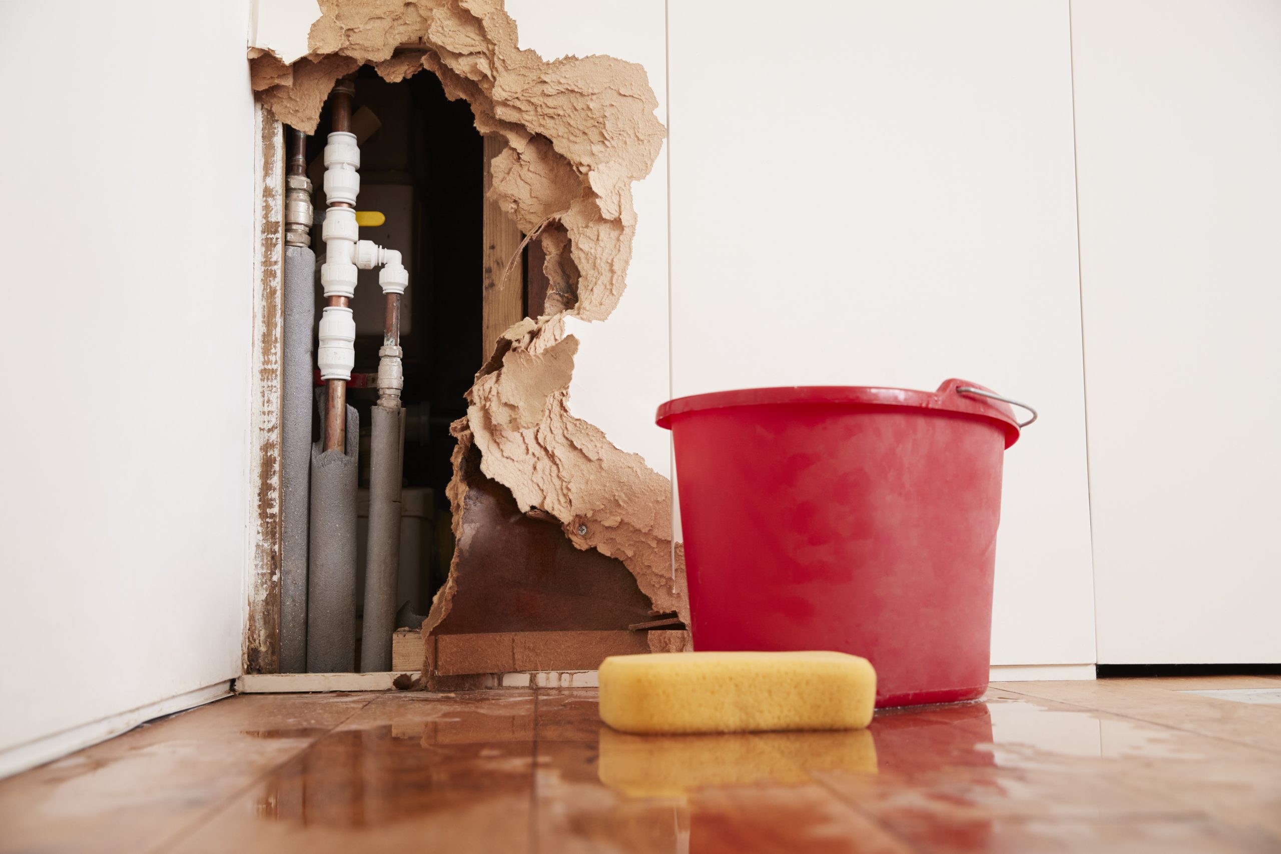 Burst pipe damage — broken wall exposing pipes with water pooled on floor, showing urgency of burst pipe cleanup