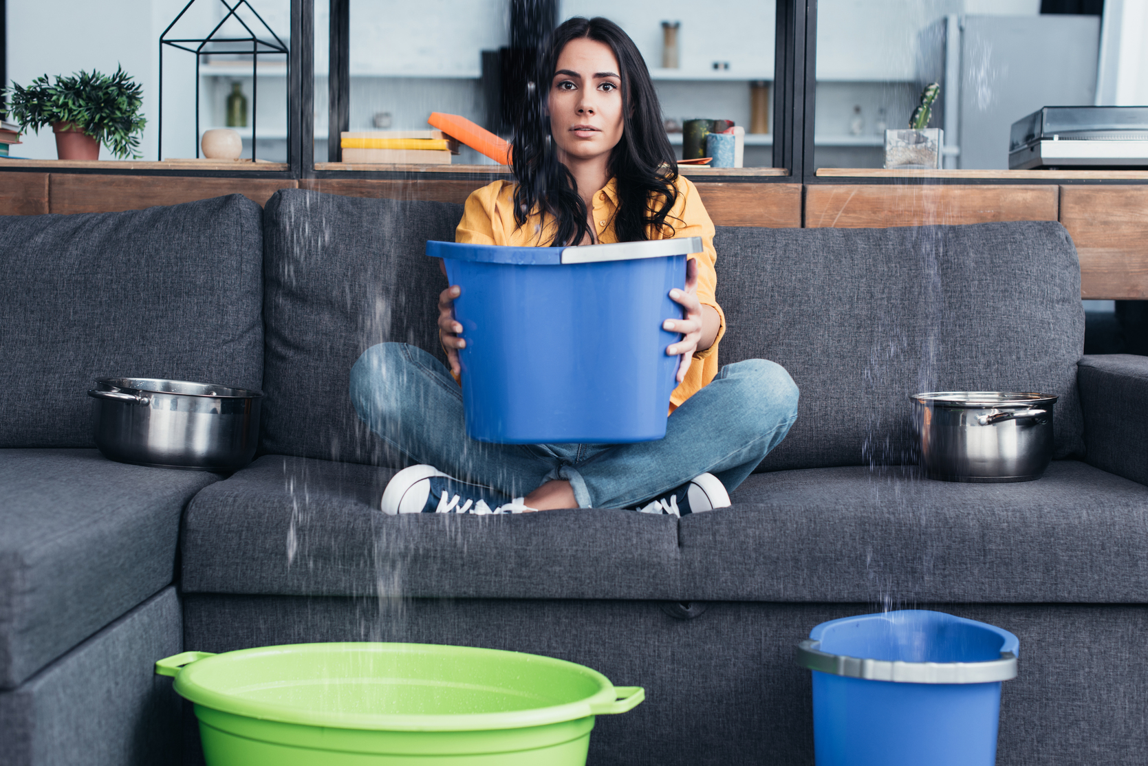 Homeowner with bucket catching water during active flood — flood damage cleanup urgency