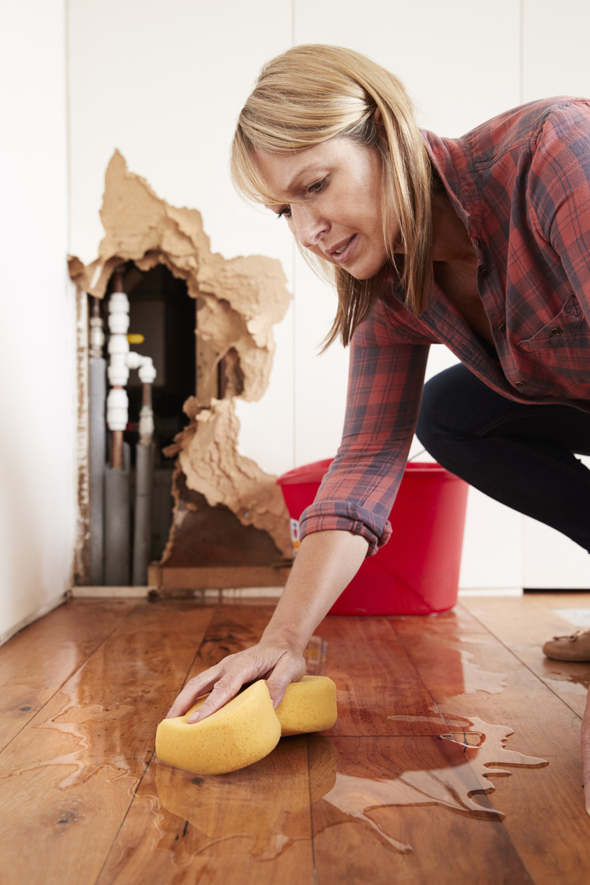 Professional water extraction — woman mopping standing water from a burst pipe in a residential home